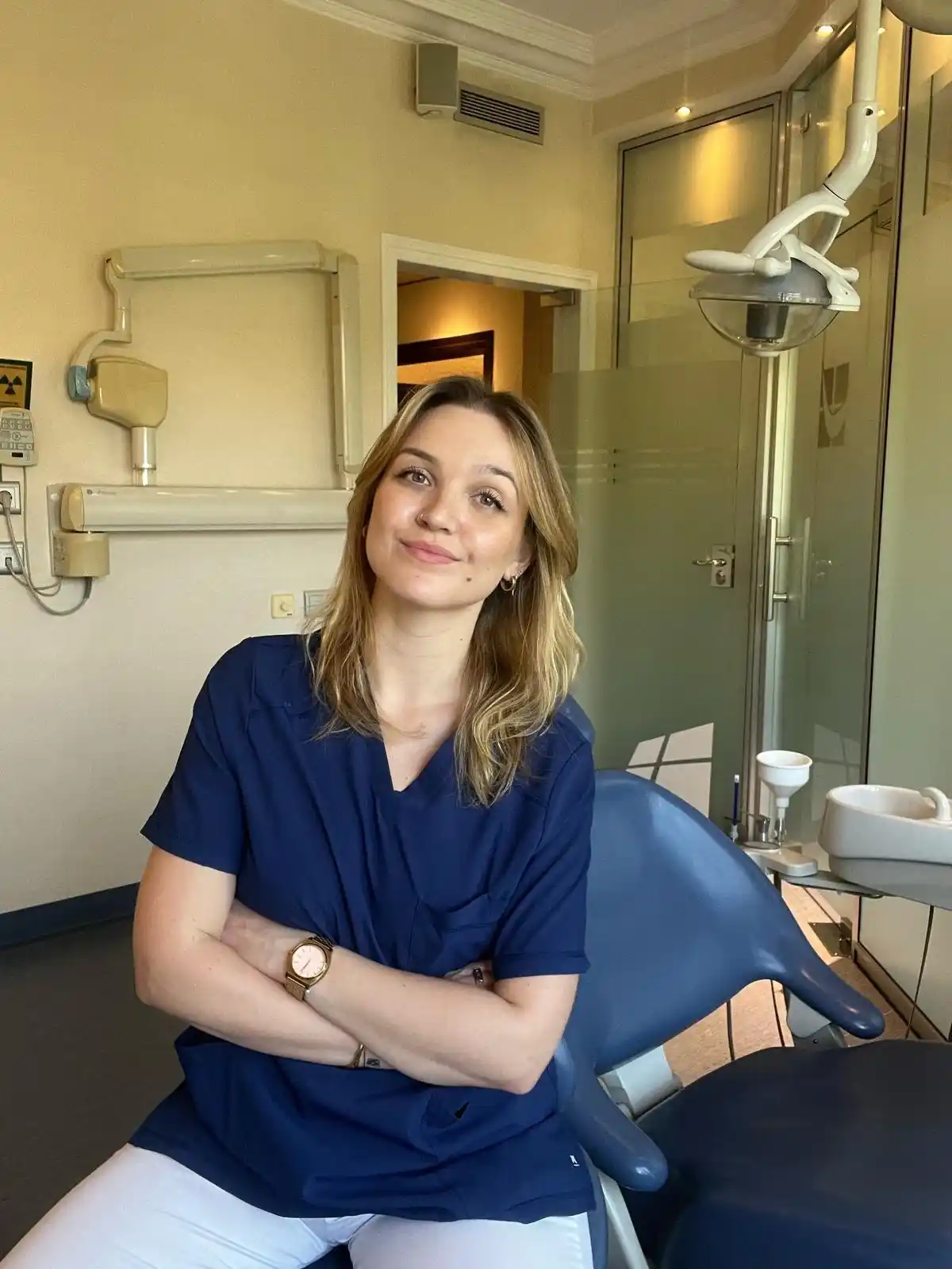 Dana, fisioterapeuta maxilofacial, sonriendo y mirando a cámara en consulta con el pelo suelto y brazos cruzados.