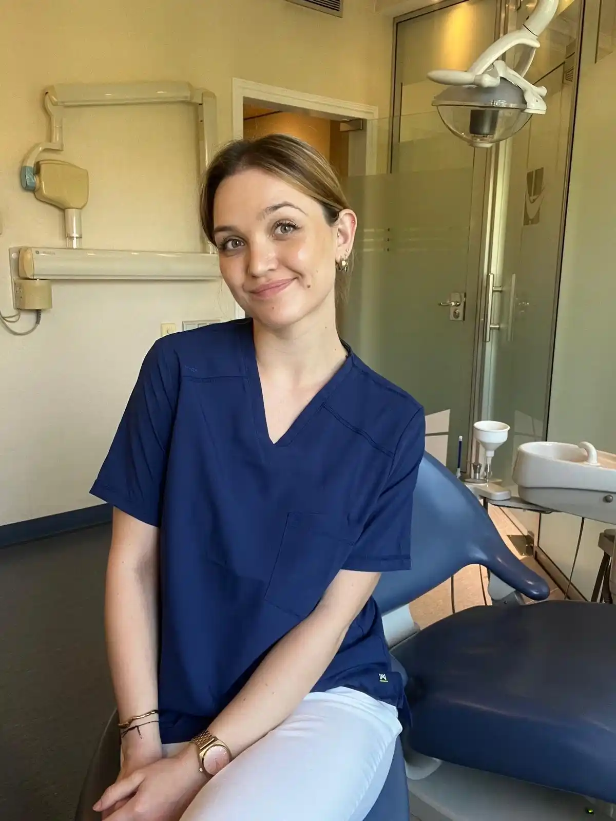 Dana, fisioterapeuta maxilofacial en Barcelona, sonriendo y mirando a cámara en consulta, con el pelo recogido